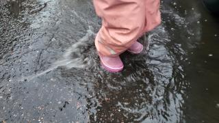 Lapsi hyppii vesilätäkössä kumisaappaat jalassa.