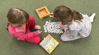 Kaksi lasta pelaa nappulapeliä lattialla istuen.