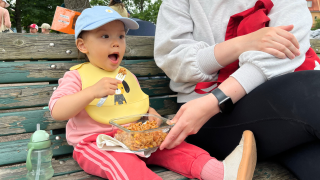 Kaksivuotias tyttö istuu puiston penkillä syömässä ruokaa.