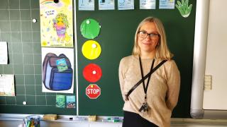 Aino seisoo luokan liitutaulun edessä.