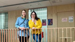 Reetta ja Irina seisovat koulun käytävällä ja nojaavat kaiteeseen.