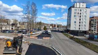 Katunäkymä Hakunilantieltä aurinkoisena päivänä, kuvassa ratikan työalueet rajattu työmaa-aidoin, kaivuri sekä autoja.