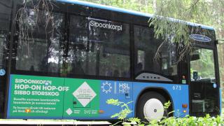 Sipoonkorven bussi metsätiellä. Sinisen bussin kyljessä vihreä Sipoonkorpi Hop-on Hop-off -teippaus.