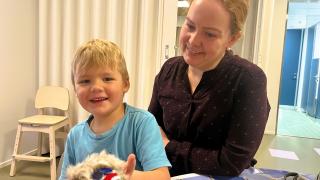 Lapsi esittelee kameralle kivestä askartelemaansa voimaeläintä yhdessä varhaiskasvatuksen opettajan kanssa.