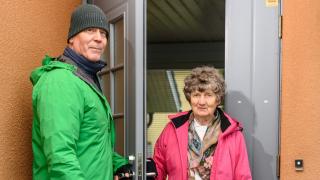 Syysvaatteisiin pukeutuneet kaksi aikuista ovensuussa, heidän edessään pieni koira.