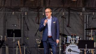 Pekka Timonen puhuu mikrofoniin konserttilavalla, taustalla soittimia.