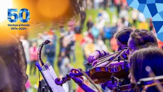 Violinister i förgrunden, lyssnare i parken i bakgrunden. Överst till höger hörnet med jubileumsårets hörnelement och till vänster hörnet med jubileumsårets emblem.