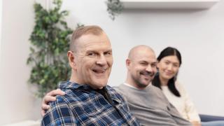 Kolme ihmistä katsovat kameraan hymyillen.