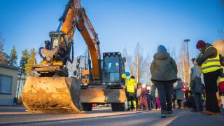 Kaivinkone, lapsia ja Vantaan ratikan työntekijöitä Rajakylän koululla järjestetyssä heijastintempauksessa.