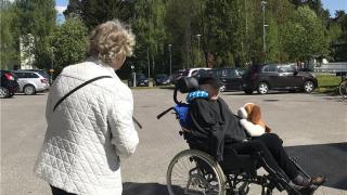 Kaksi henkilöä josta toinen pyörätuolissa odottaa tapaamisautoa.