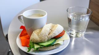 Sämpylä, teemuki ja vesilasi pöydällä.