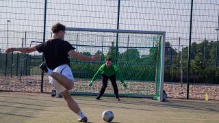 Pelaaja on potkaisemassa palloa kohti maalia ja maalivahti valmistautuu torjumaan maalin.