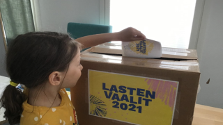 Lapsi tiputtaa äänestyslipukkeen laatikkoon.