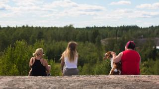 Kolme ihmistä ja koira istuvat kalliolla.
