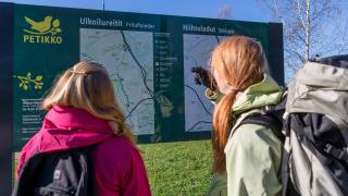 Kaksi ihmistä katselemassa Petikon luontovirkistysalueen ulkoilureittien ja hiihtolatujen opastetaulua.