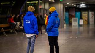 Tikkurilan asemalla seisoo kaksi nuorisotyöntekijää, joilla siniset takit, joissa Nuorten Vantaa -teksti.