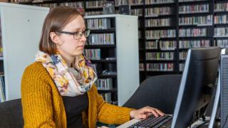 A woman is sitting at a computer in a library.