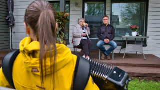 Nainen soittamassa haitaria kahdelle ihmiselle talon takapihalla.