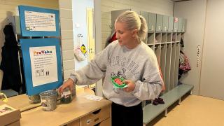 Nelli seisoo päiväkodin tiloissa ja näyttää lelusammakoita ja kuulapurkkeja.