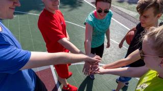 Nuoret laittavat kannustushuutoa varten kädet ringissä päällekkäin koripallokentällä.