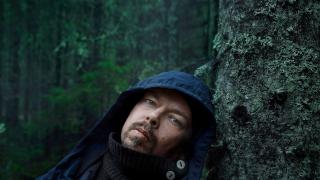 Perttu Saksa nojaa puuhun metsässä
