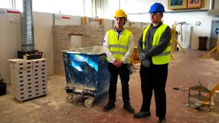 Santtu ja Sarvarbek talonrakennushallissa. He ovat pukeutuneet huomioliiveihin, suojalaseihin ja kypäriin.