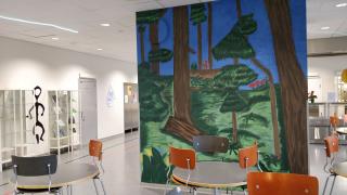 Rekolanmäen koulun ruokala. Ruokalan keskellä on seinä, johon on maalautta kuva metsästä.