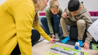 Opettaja ja kaksi lasta kumartuneina ohjelmointipelin ääreen.