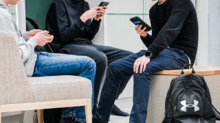 Kolme oppilasta istuu tuoleilla puhelimet kädessä.