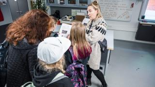 Kaksi aikuista ja kolme innokasta lasta luokkahuoneessa. Yksi lapsista pitelee paperia, jonka ympärille kaikki ovat kerääntyneet.