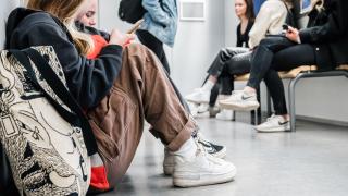 Nuoria istumassa koulun käytävällä selaamassa puhelinta.