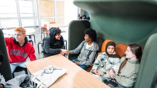 Nuoria henkilöitä istumassa pöydän ääressä ja juttelemassa.