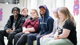 Kuusi hymyilevää nuorta istuu rivissä.