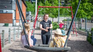 Varhaiskasvatuksen opettaja keinuttaa lapsia pihalla.