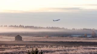 Sumuinen peltomaisema auringonnousun aikaan. Lentokone lentää kaukana taivaalla.