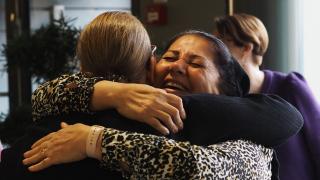 Kaksi henkilöä halaavat hymyillen.