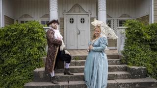 Nainen ja mies 1700-luvun asuissa kartanon portailla