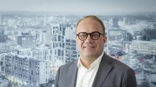 Pekka Timonen hymyilee. Taustalla näkyy kaupunkikuvaa.