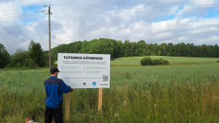 Tutkimushanke käynnissä -kylttiä pystytetään pellolle.