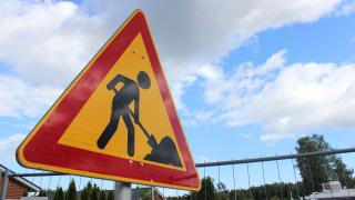 Työmaakyltti, jonka taustalla näkyy sininen taivas ja pilviä.