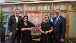 Viisi ihmistä seisovat muotokuvan ympärillä