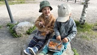 Kaverukset Viljo ja Lenni syövät puistoruokailussa kivellä istuen.