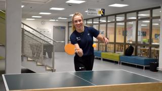 KouluPT-ohjaaja Anni pelaa hymyillen pingistä koulun aulassa.