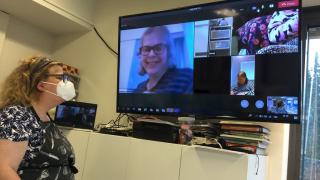 Etätapaaminen Teams välityksellä, huoneessa ja TV:ssa näkyvät hymyilevät ihmiset.