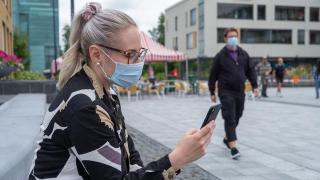 henkilö kätso kännykkään maski kasvolla.