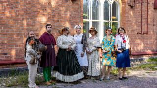 Henkilöitä eri aikakausien vaatteissa museon edustalla 