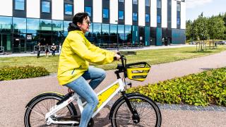 Nainen pyöräilee keltaisessa takissa.