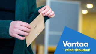 ruskea kirjekuori käsissä ja sininen logo oikeassa alakulmassa vantaa-minä sitoudun!