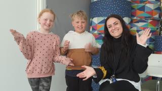läraren och två elever vinkar glatt