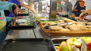 Oppilaat ottavat ruokaa linjastolta. Tarjolla on muun muassa omenaa ja ruisleipää.